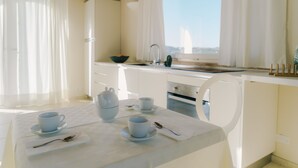 A bright, modern kitchen with white cabinetry, a dining table set with cups and a spoon, and a view of the city through large windows. - Rent exclusive Villa Nontiscordar with pool in Marche (Civitanova Marche)