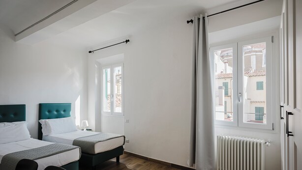A hotel room with two beds, a radiator, and a window with a view of buildings.