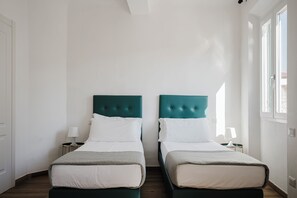 A hotel room with two single beds, each with a white pillow and a grey blanket. There are bedside tables with lamps, and the room has white walls and a wooden floor. - Alloro Apartment - Three Bedroom Apartment, Sleeps 6 (Firenze)