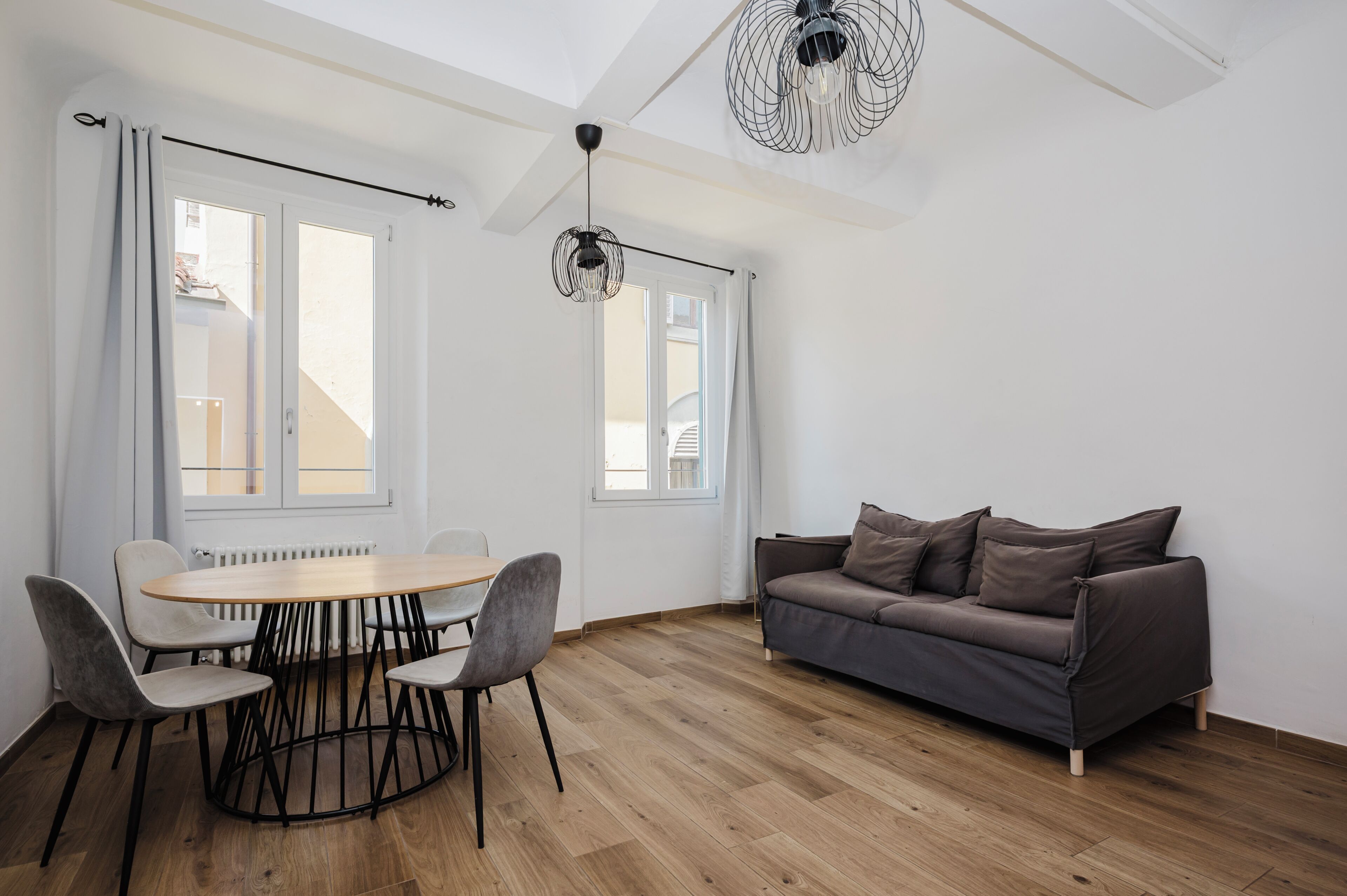 Un espace de vie moderne avec une table ronde en bois, des chaises à revêtement gris, un canapé gris et un ventilateur de plafond original.