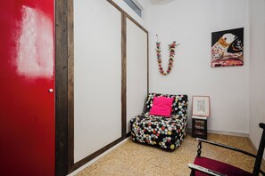 Una habitación con una puerta roja, una pequeña silla con un cojín estampado de lunares de colores, un adorno con forma de pájaro montado en la pared y un cuadro enmarcado.