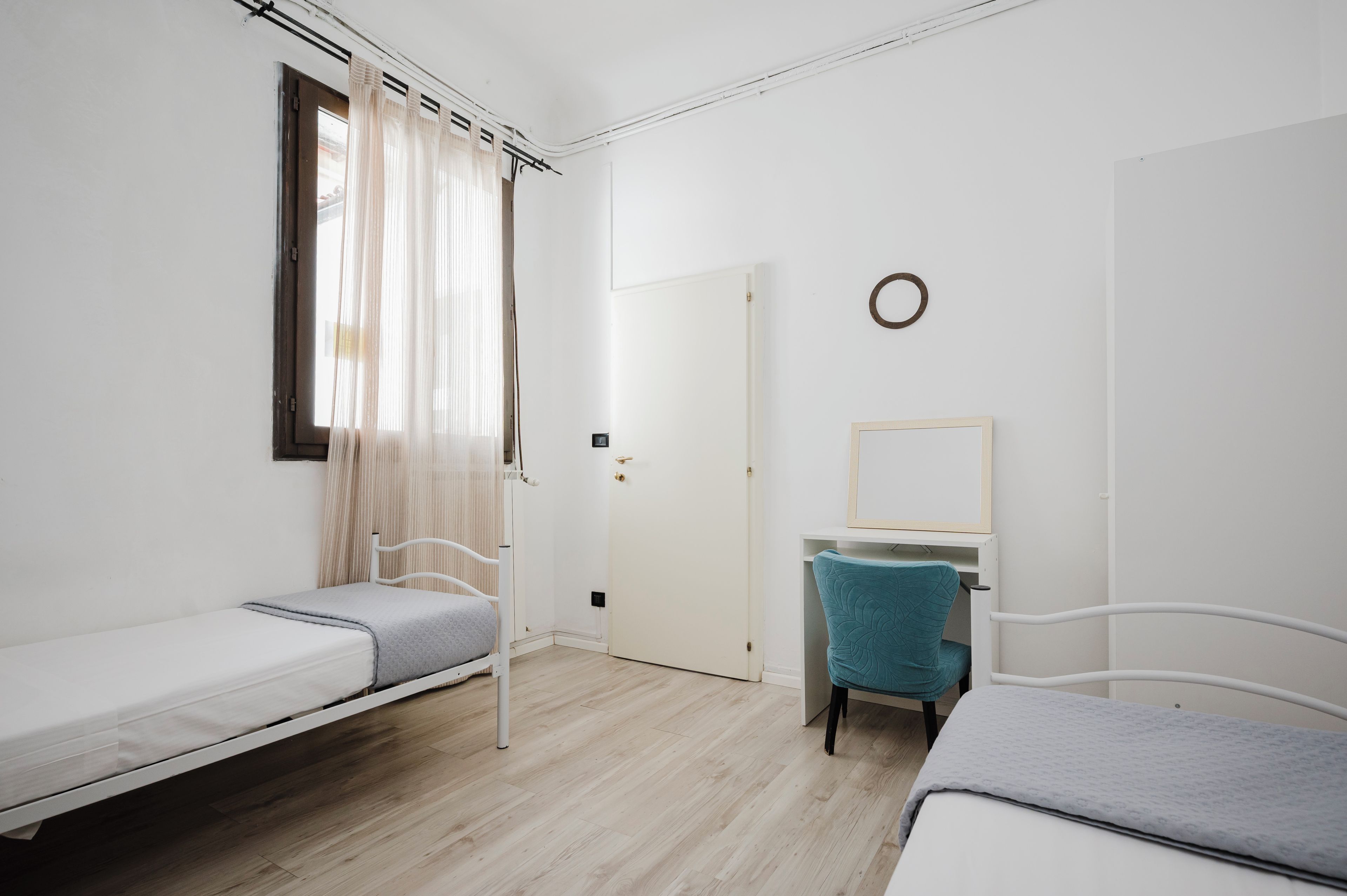 A simple, clean room with two single beds, a chair, a small desk, and a door.
