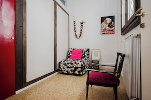 A narrow hallway with a red door, a small seating area with a polka dot cushion, and a framed artwork on the wall.