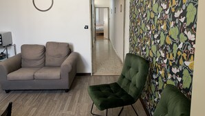 Una sala de estar con un sofá, un sillón verde, un televisor y una pared con diseño.