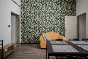 Ein Zimmer mit gemustertem Wandpapier, einer hölzernen Bank, einem gelben Sessel und einem Tisch mit Platzsets.