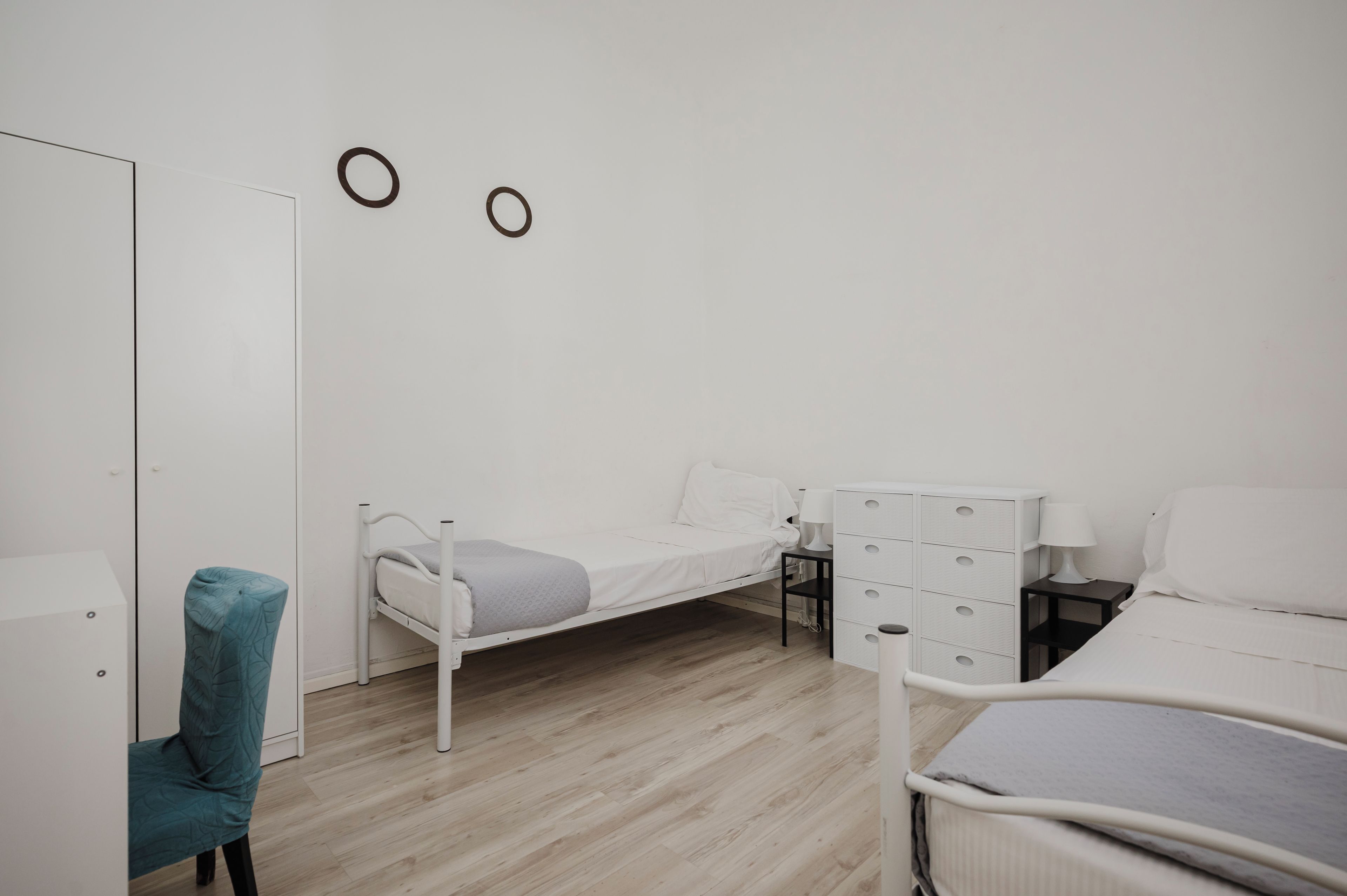 A minimalist bedroom with a single bed, a small bedside table, a chair, and a wardrobe.