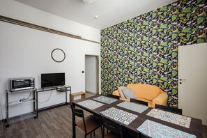 A modern room with a kitchenette, a television, a patterned wall, and a sofa.