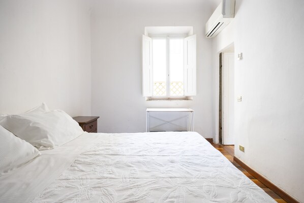 Un dormitorio con cama, mesita de noche, ventana y equipo de aire acondicionado.