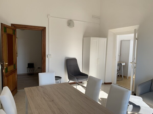 Une pièce moderne avec une table à manger en bois, des chaises blanches, un fauteuil gris et une armoire blanche.