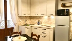 A compact kitchen with white cabinets, a microwave, a refrigerator, and a dining table with chairs. - Martiri del Popolo 28 (Firenze)
