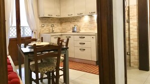 A compact kitchen with white cabinets, a tiled backsplash, and a dining area with a table and chairs. - Martiri del Popolo 28 (Firenze)