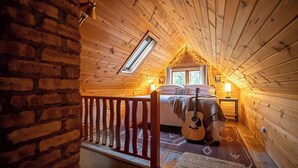 A cozy attic bedroom with a wooden ceiling, a skylight, a bed, a guitar, and a small table with a lamp. - Secluded in the Woods, Hot Tub (Twin Lakes)