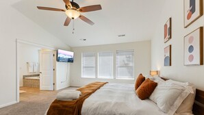 Ein Schlafzimmer mit einem Bett, einem Deckenventilator, einem Fernseher und einem Fenster mit Jalousien.