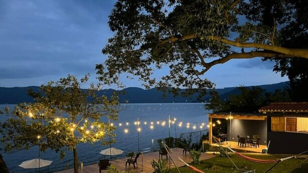 Ein Anwesen am Seeufer mit einer Terrasse, Sitzgelegenheiten im Freien und Lichterketten.