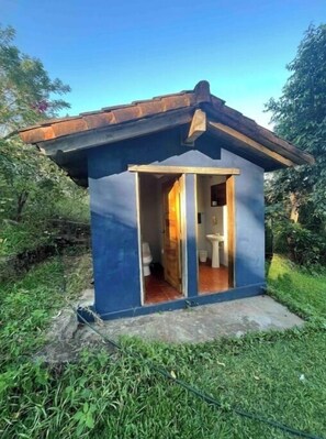 a restroom with a toilet and sink, nestled among trees in a secluded area.