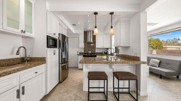 A modern kitchen with white cabinets, granite countertops, stainless steel appliances, and a central island with stools.