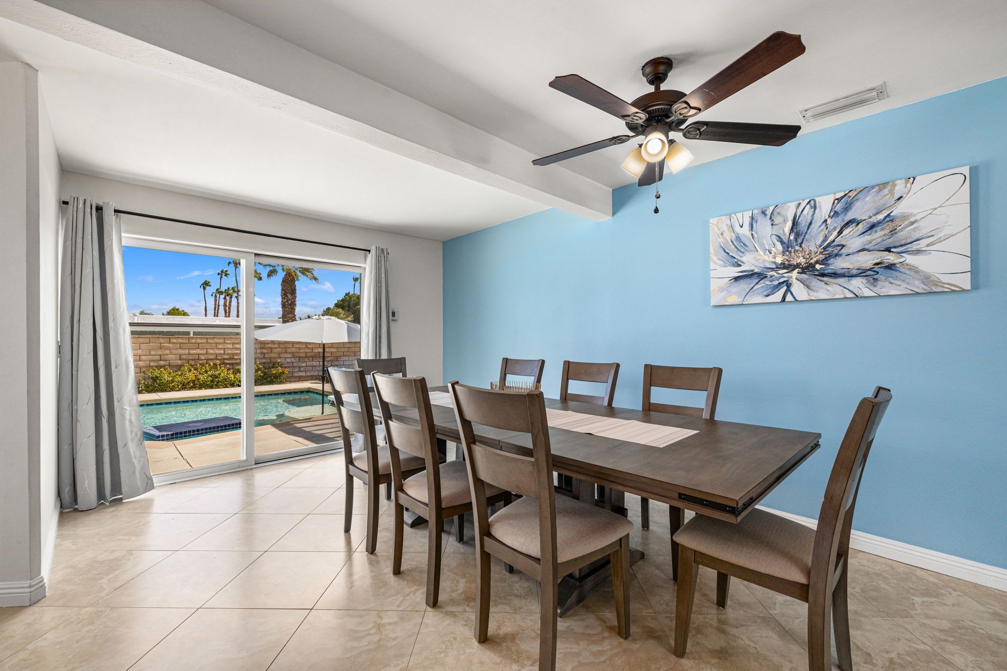 A dining area with a table and chairs, a ceiling fan, and a view of a swimming pool through glass doors.