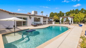 A backyard with a swimming pool, a patio area, and a pergola.