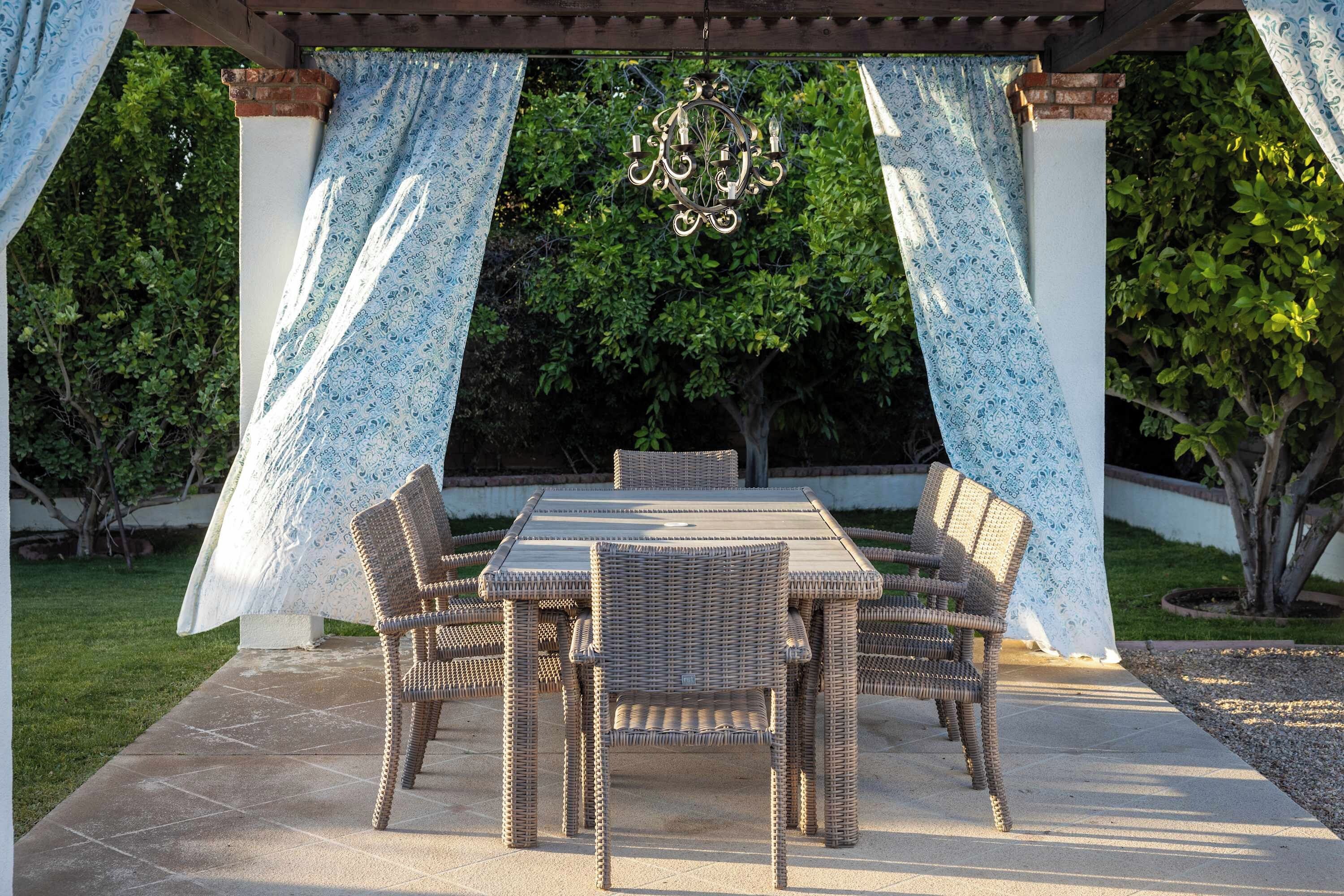 An outdoor patio with a table and chairs, surrounded by patterned curtains and a hanging light fixture.