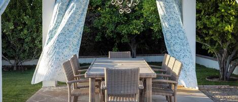 An outdoor patio with a table and chairs, surrounded by patterned curtains and a hanging light fixture.