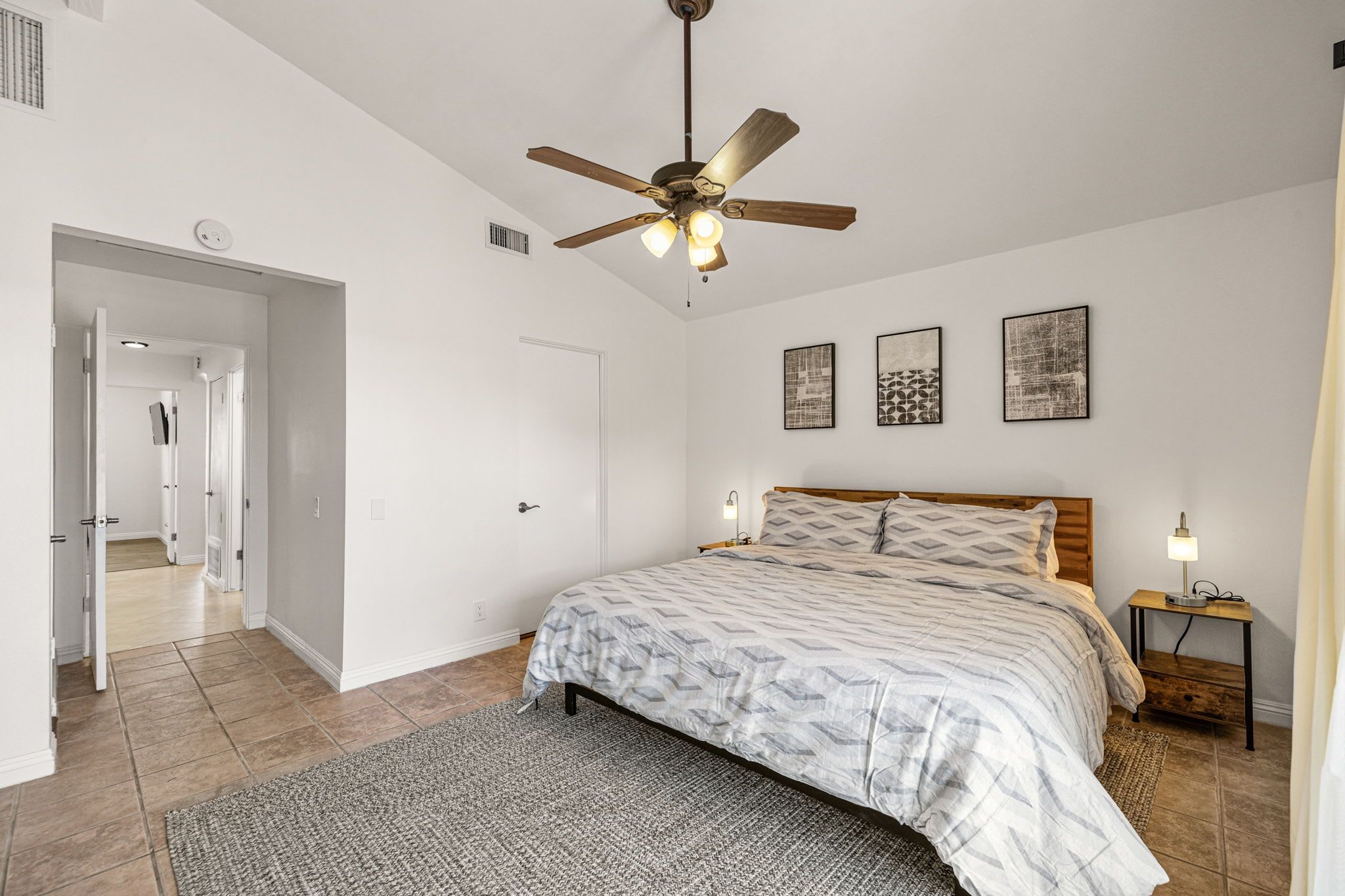 A bedroom with a bed, a ceiling fan, a nightstand, and a door leading to another room.