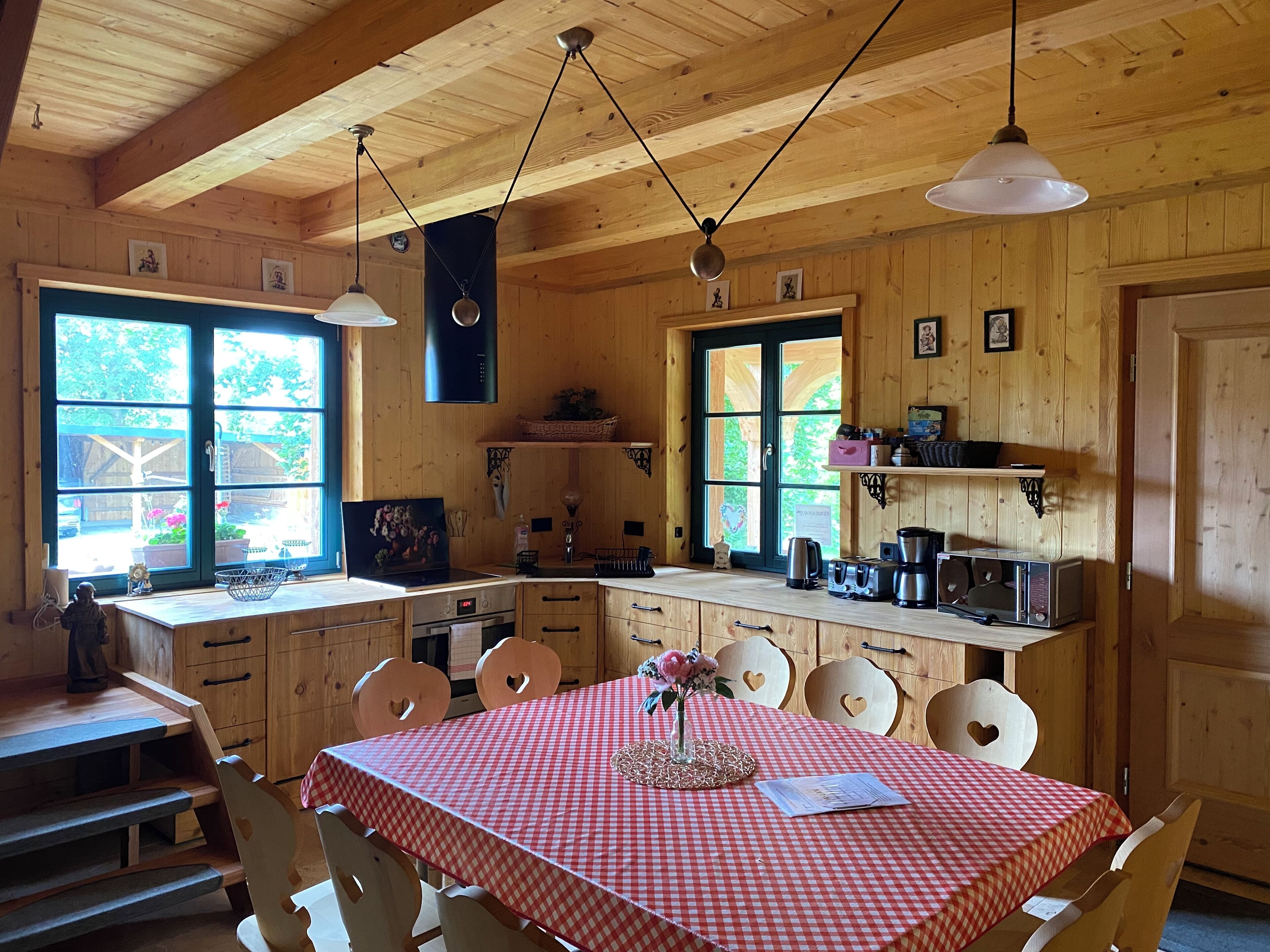 Puinen mökki, jonka sisätiloissa on keittiö, ruokailutila ja suuret ikkunat.