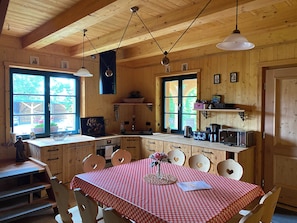 Puinen mökki, jonka sisätiloissa on keittiö, ruokailutila ja suuret ikkunat.