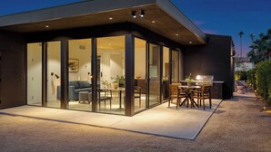 Ein modernes Haus mit einer verglasten Patio-Terrasse, einem Esstisch und Stühlen.