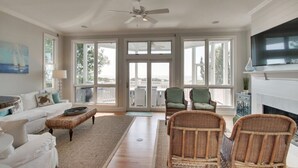 A spacious living room with a large window, a ceiling fan, a fireplace, and a television. - 45 Ocean Point by Avantstay Amazing Views + Beach Access & Community Pool Access (Isle of Palms)