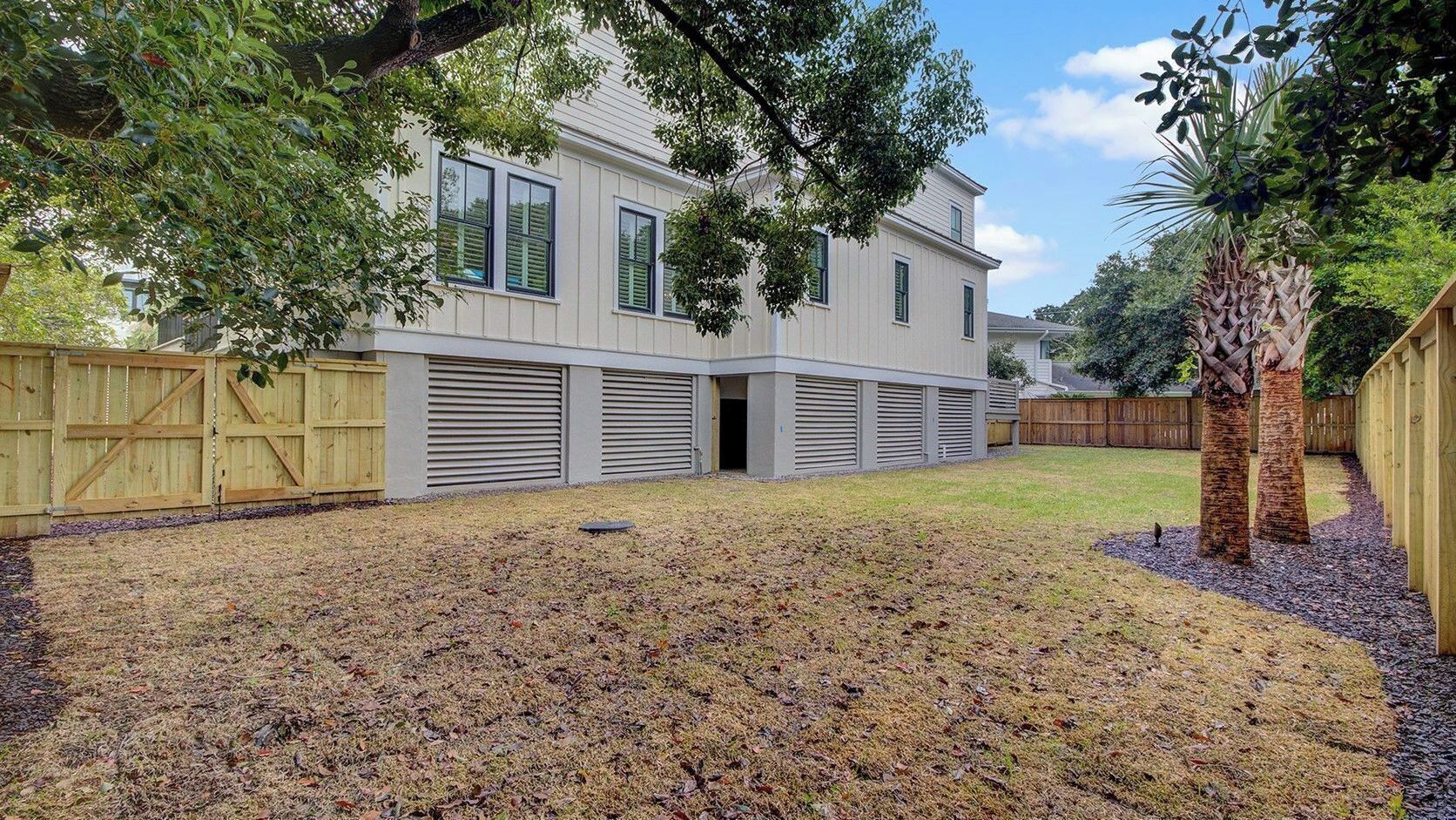 A two-story house with a covered garage, a fenced yard, and a palm tree.