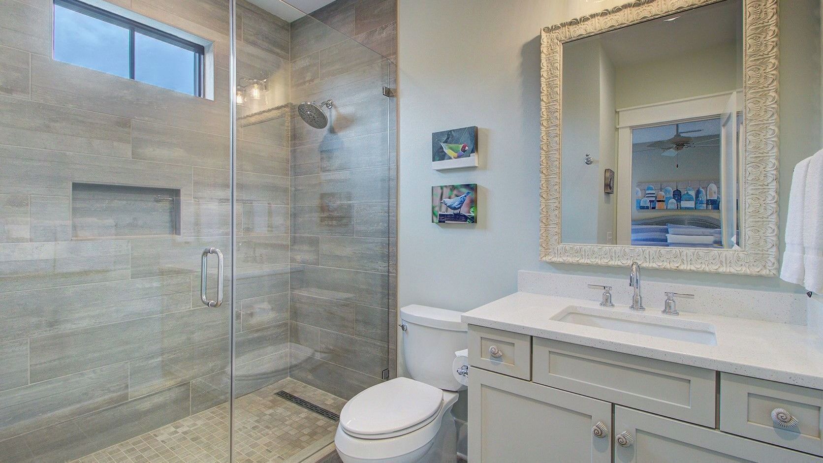 A modern bathroom with a glass-enclosed shower, a white toilet, a vanity with a mirror, and artwork on the wall.