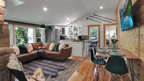 A modern kitchen with white cabinets, a dining area with a wooden table set for four, and a living room with a brown leather sofa and a fur rug. - Lake, Golf & Hike at Linville Lodge in  Linville  Land  Harbor  Resort Community (Newland)