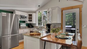 A modern kitchen with white cabinets, stainless steel appliances, and a wooden dining table set for four. - Lake, Golf & Hike at Linville Lodge in  Linville  Land  Harbor  Resort Community (Newland)