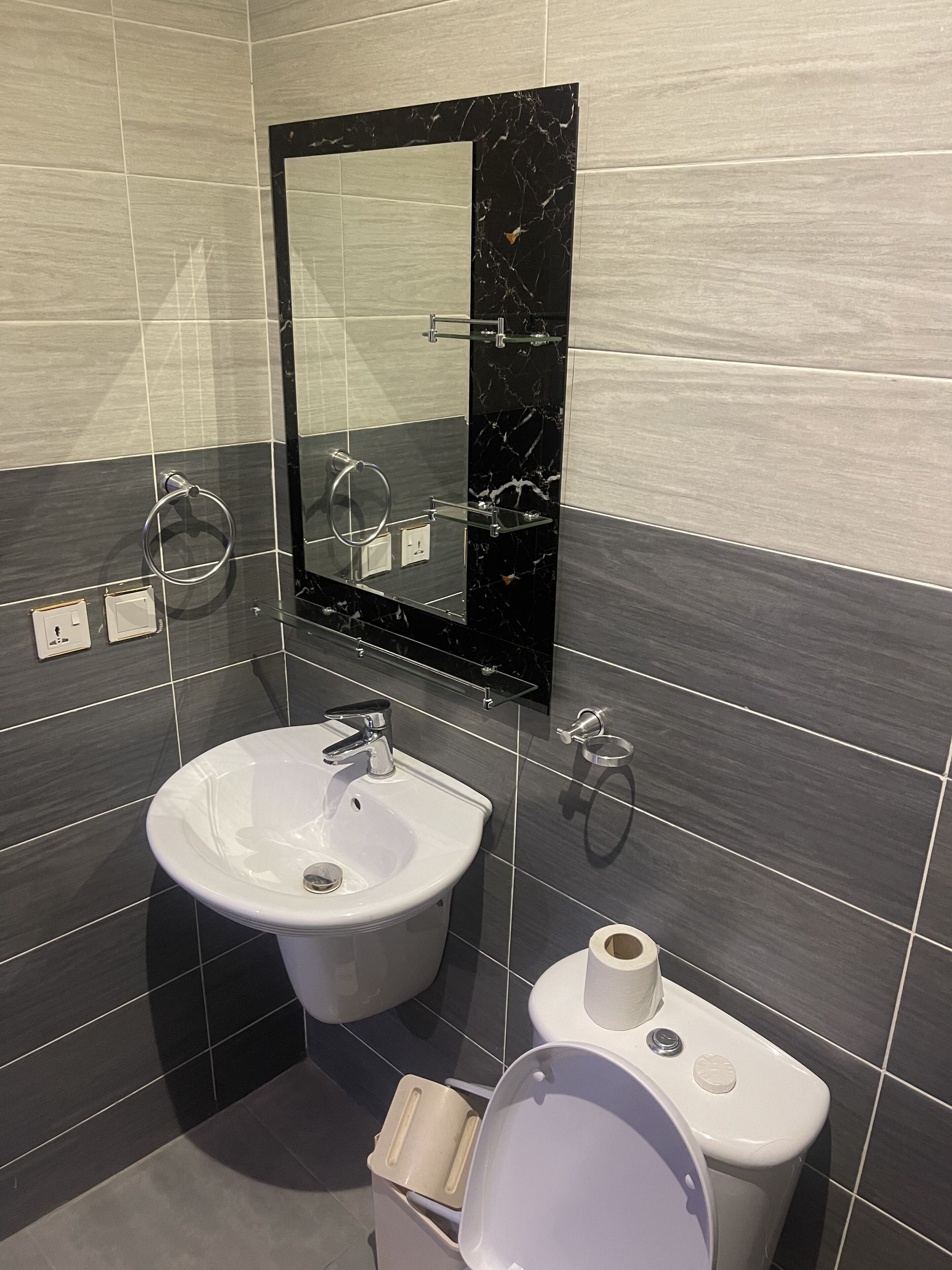 Un baño moderno con lavamanos blanco, salpicadero de mármol negro y un espejo grande.