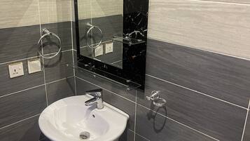 Un baño moderno con lavamanos blanco, salpicadero de mármol negro y un espejo grande.