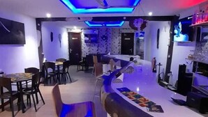 A modern bar area with a curved counter, blue lighting, and a seating area with tables and chairs. - LOYALTY HOTEL  (Accra)