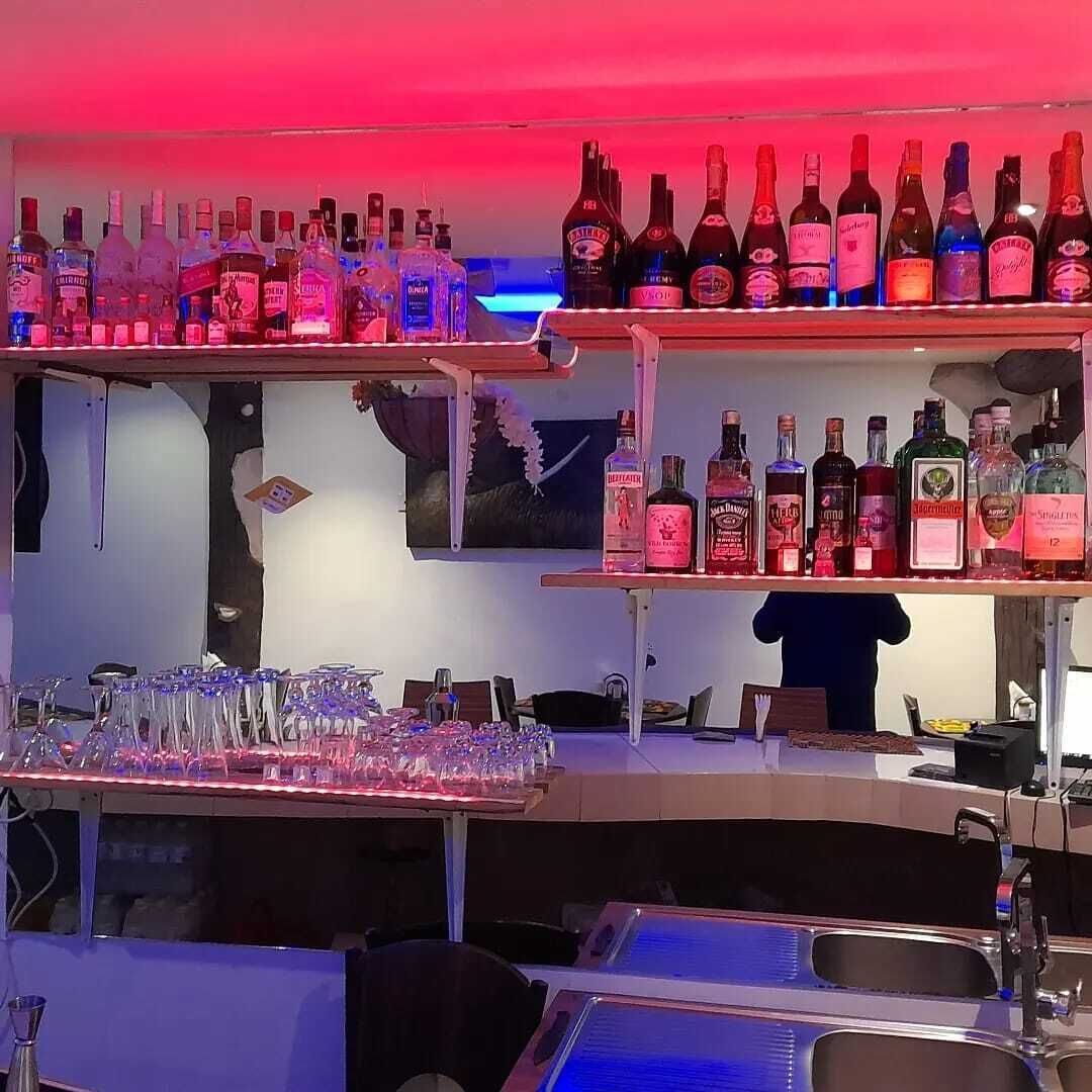 A bar area with shelves of liquor bottles, glasses, and a bar counter.