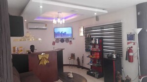 A hotel reception area with a TV, a reception desk, a fire extinguisher, and a closed shutter door. - LOYALTY HOTEL  (Accra)