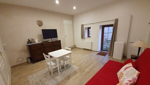 A compact living space with a dining area, a red sofa, a television, and a window with curtains.