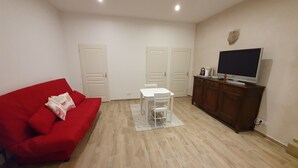 A living room with a red sofa, a small white table, and a TV on a wooden cabinet.