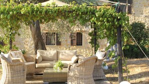 Un edificio de piedra con un patio jardín que incluye mobiliario de mimbre y una pérgola cubierta de hiedra.