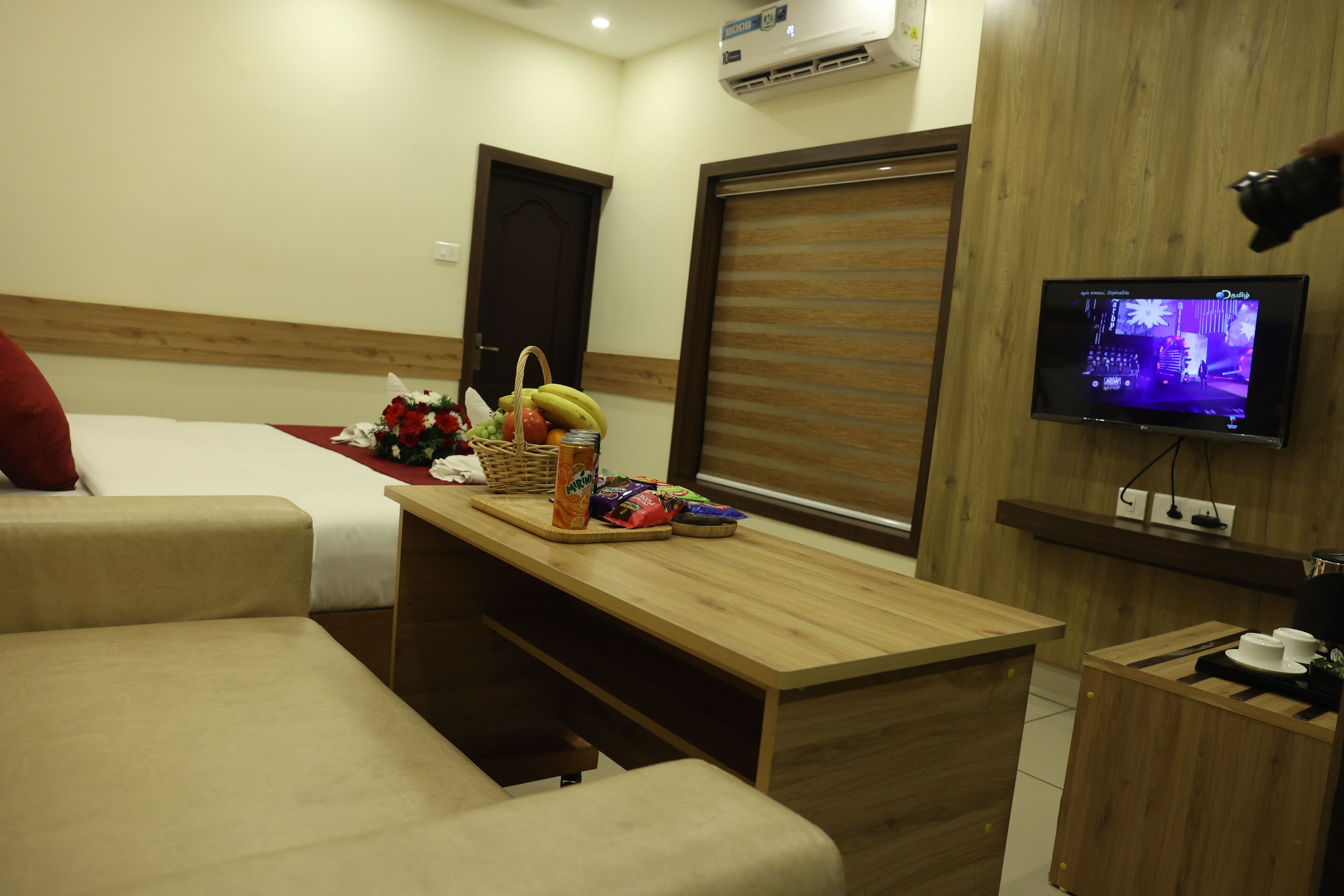 A hotel room with a bed, a wooden desk, a television, and a small table with snacks.