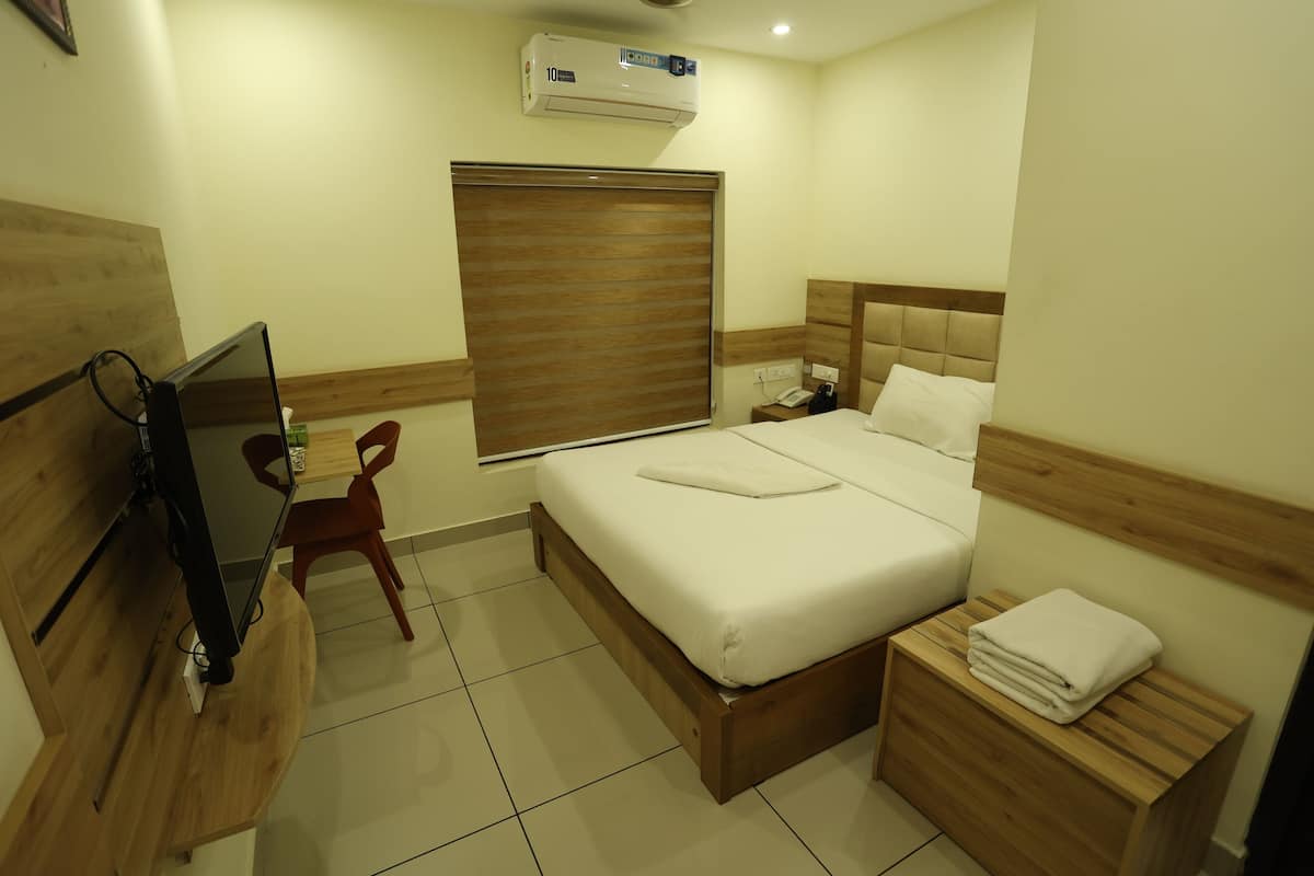 Ein Hotelzimmer mit Bett, Nachttisch aus Holz, Schreibtisch mit Stuhl und Fernseher.