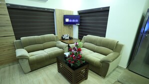 Una sala de estar con dos sofás color beige, una mesa de centro con un centro de mesa floral, un televisor de pantalla plana en la pared y un mueble de madera.