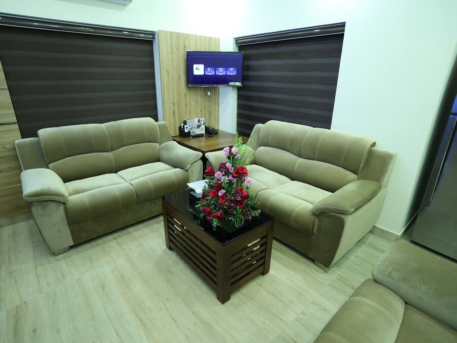 A living room with two beige sofas, a coffee table with a floral centerpiece, a flat-screen TV on the wall, and a wooden cabinet.