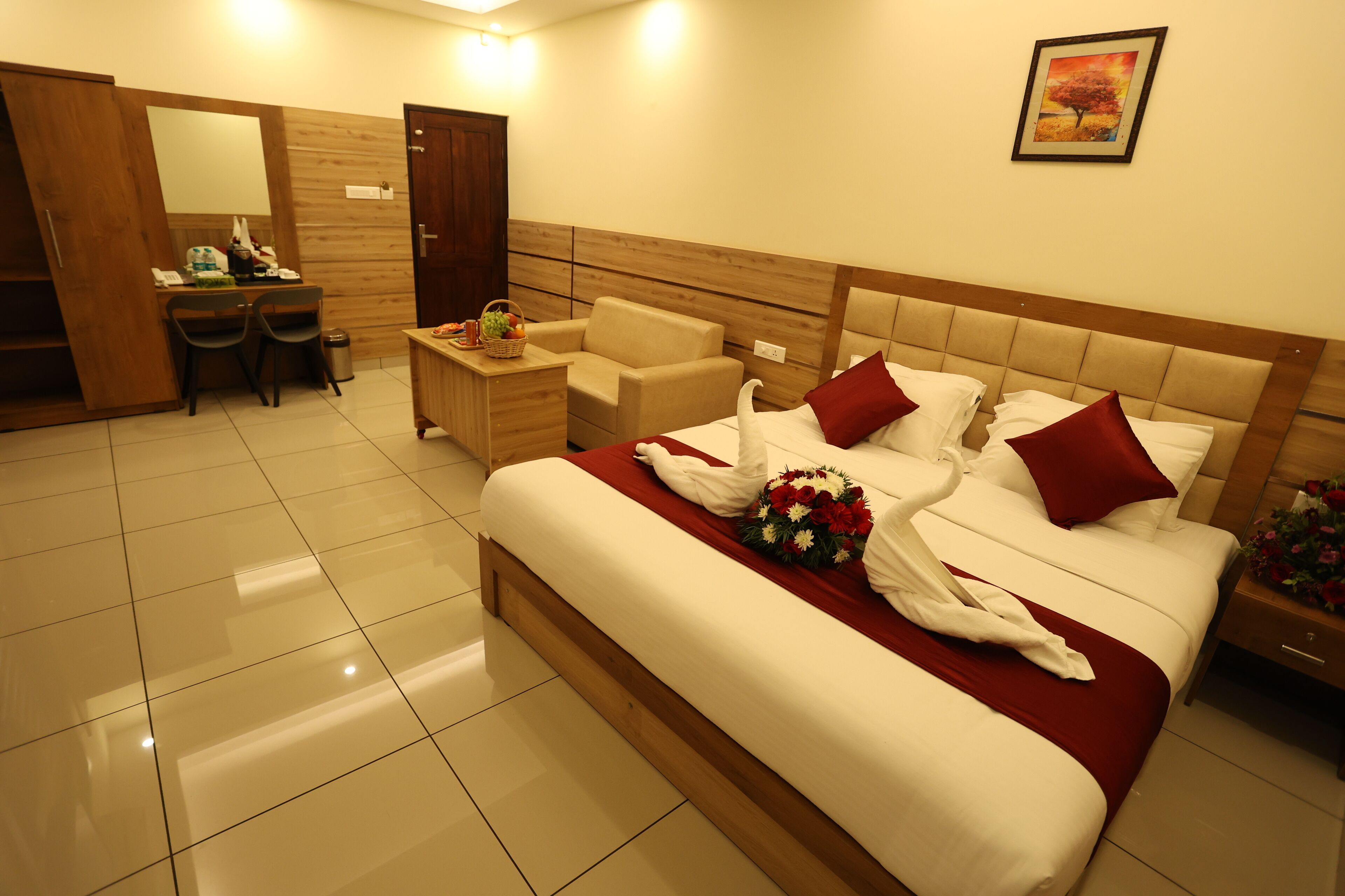 A hotel room with a large bed, a desk with chairs, a wooden wardrobe, and a wall-mounted picture.