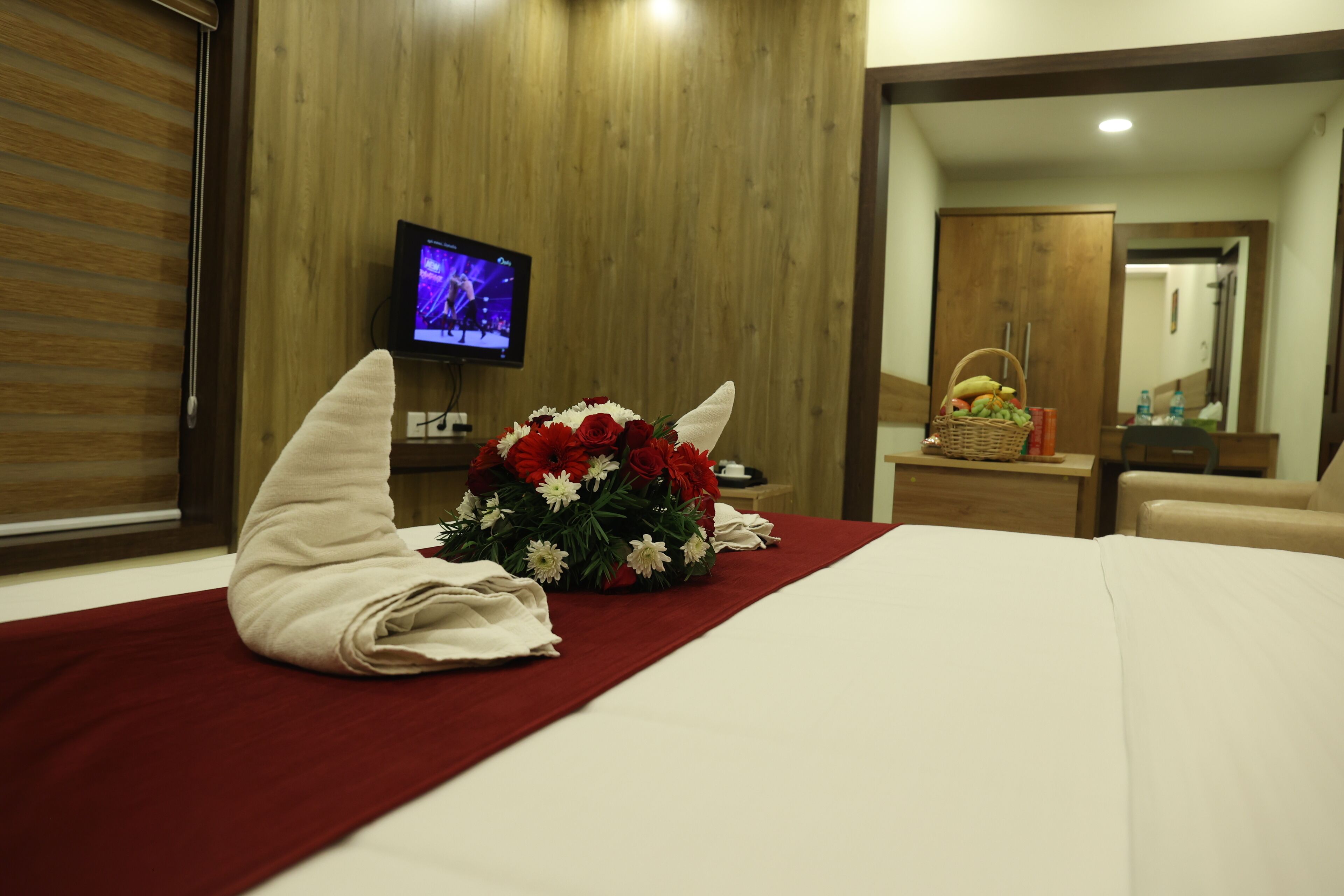 A hotel room with a neatly made bed, a bouquet of flowers, a television, and a wooden wardrobe.