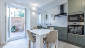 Una cucina moderna con un tavolo e sedie bianchi, forno a incasso e una porta scorrevole in vetro che dà su un patio con piante.