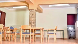 A conference room with wooden tables and chairs, a stone pillar, and a red accent wall. - Rovers Place Hotel  (Ahero)