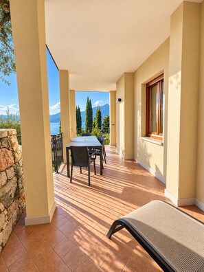 Una veranda riparata con tavolo e sedie, vista sul mare e un muro in pietra.